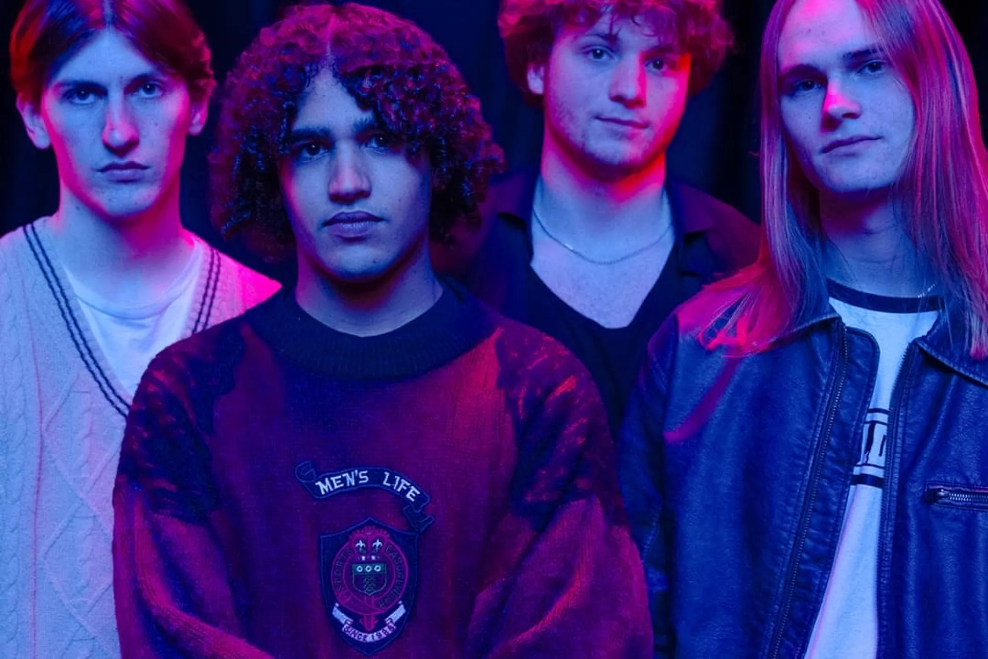 De vier leden van Bliss poseren in roze spotlight voor de camera. 