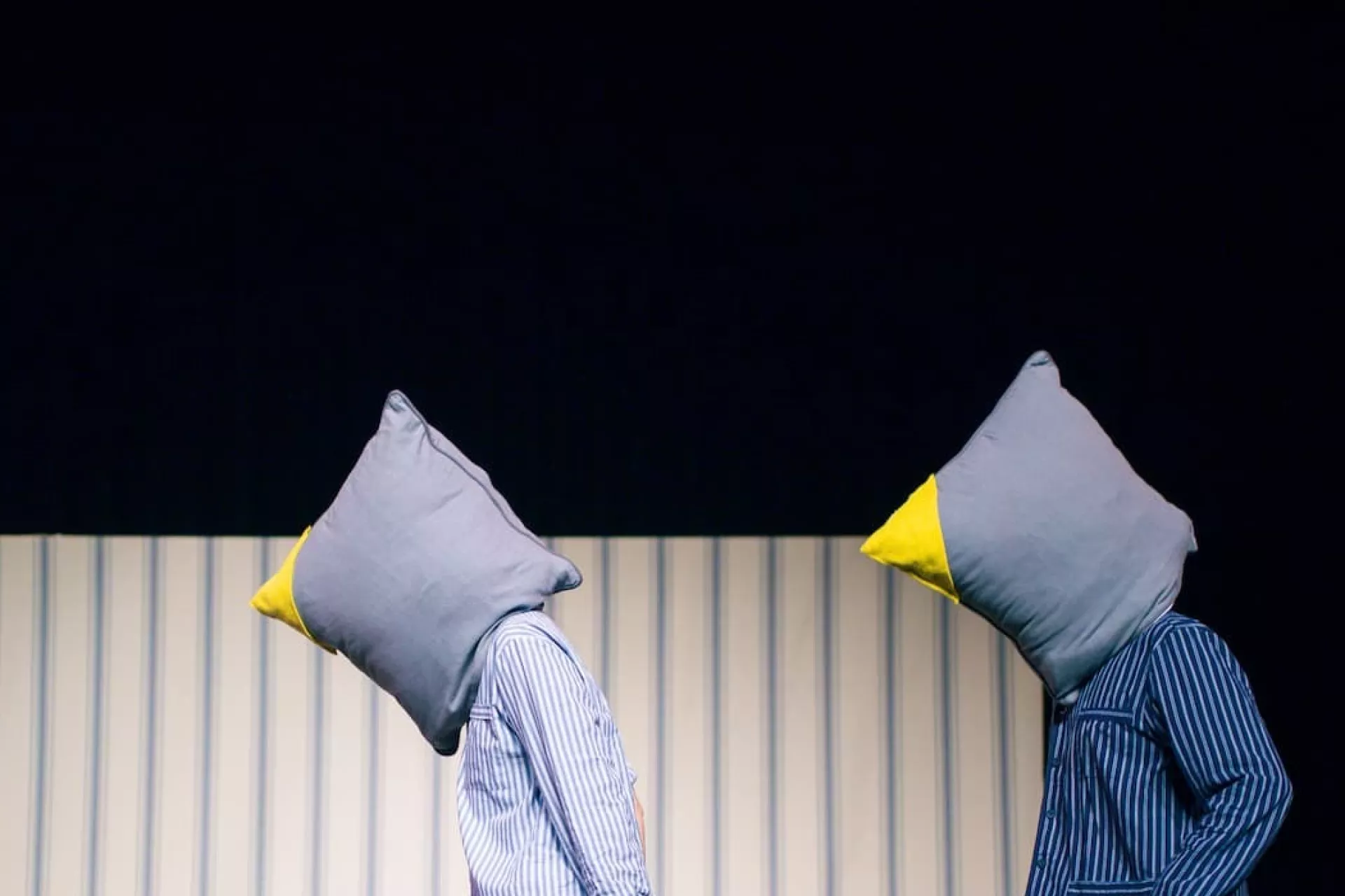 twee mannen met een kussen over hun hoofd lopen van rechts naar links op het podium in twee blauwe pyjama's 