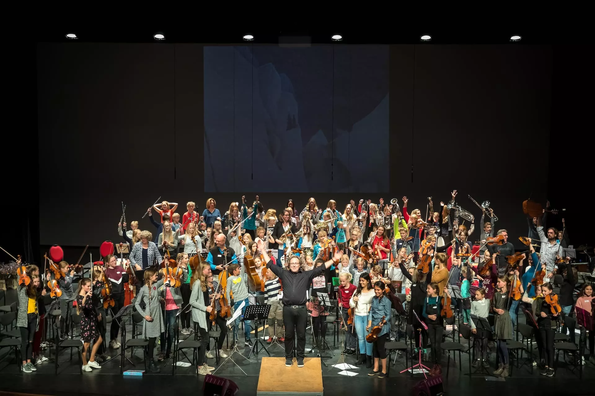 Een groot orkest met koor en de dirigent buigen voor publiek
