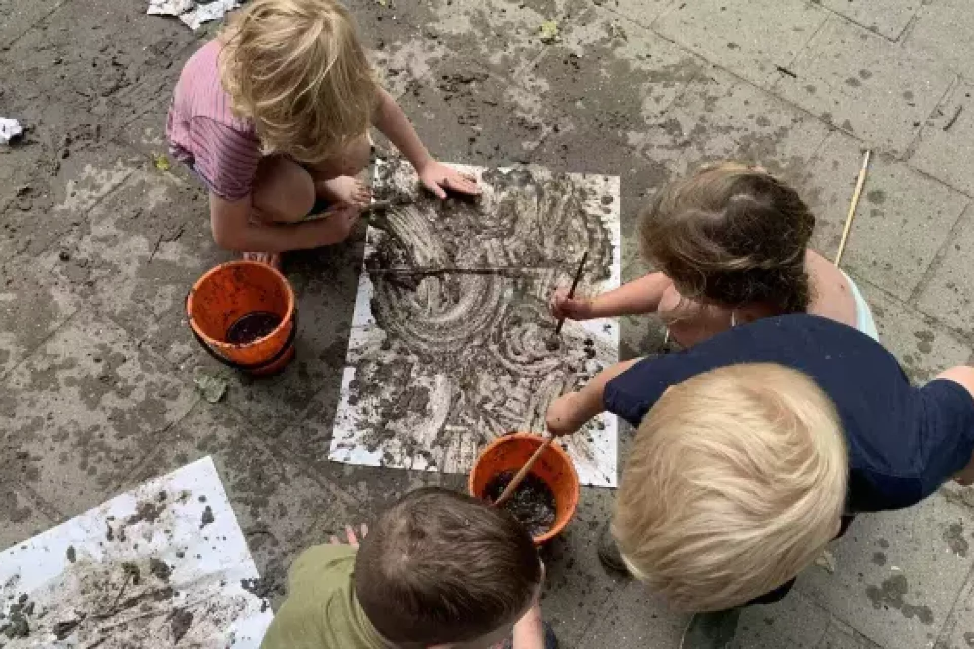 Kinderen maken kunst met modder op papier.