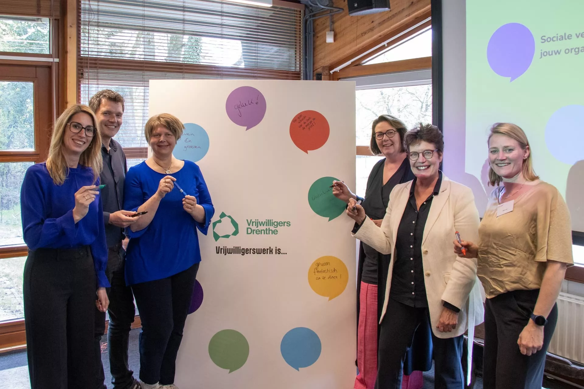 Groep mensen poseert voor een bord met kleurrijke stippen.