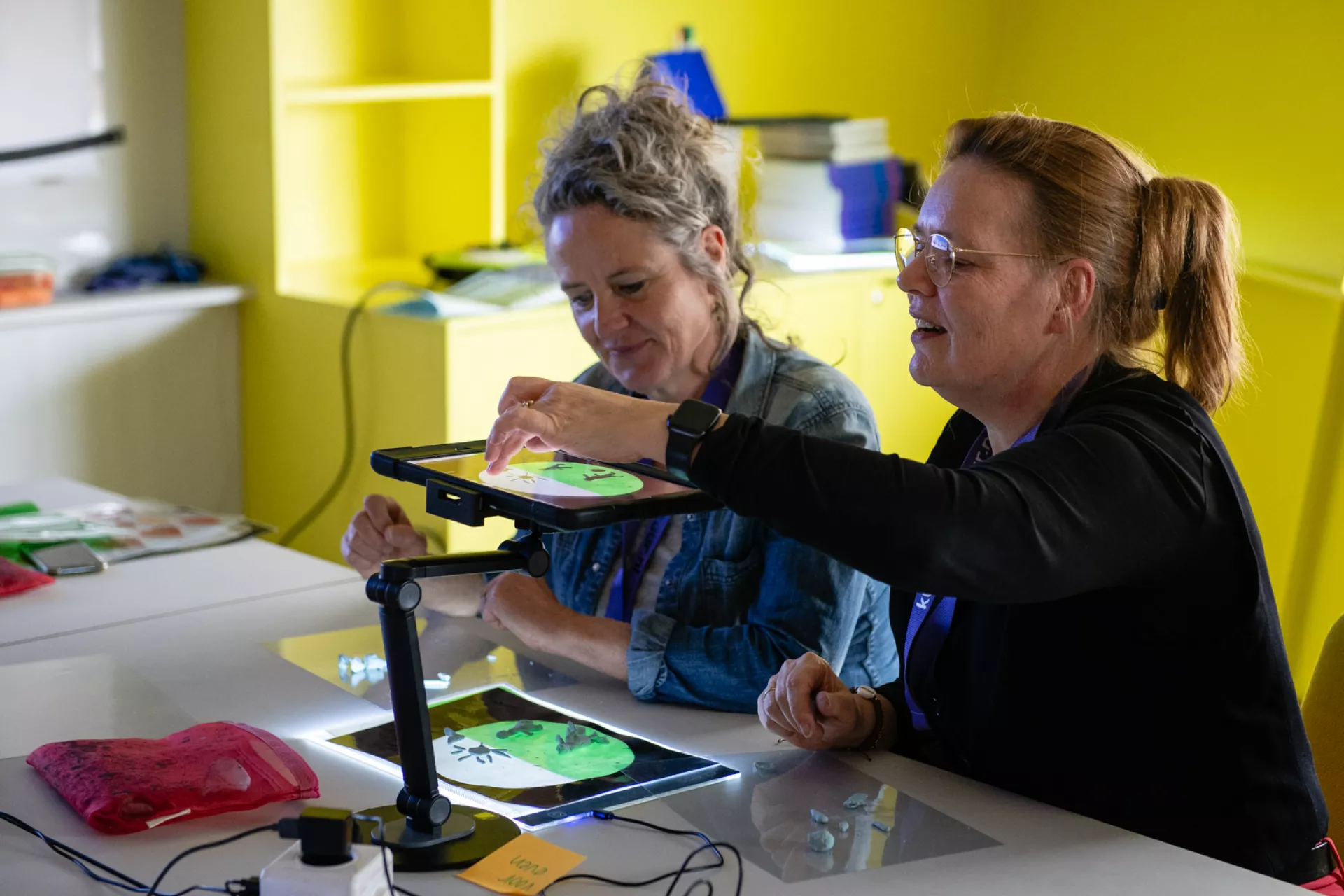 Twee vrouwen werken samen aan een project met behulp van een tablet in een creatieve ruimte.