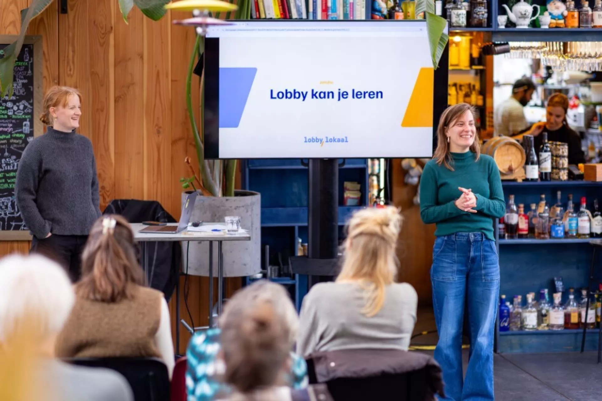 Een spreker presenteert voor een klein publiek in een informele ruimte.