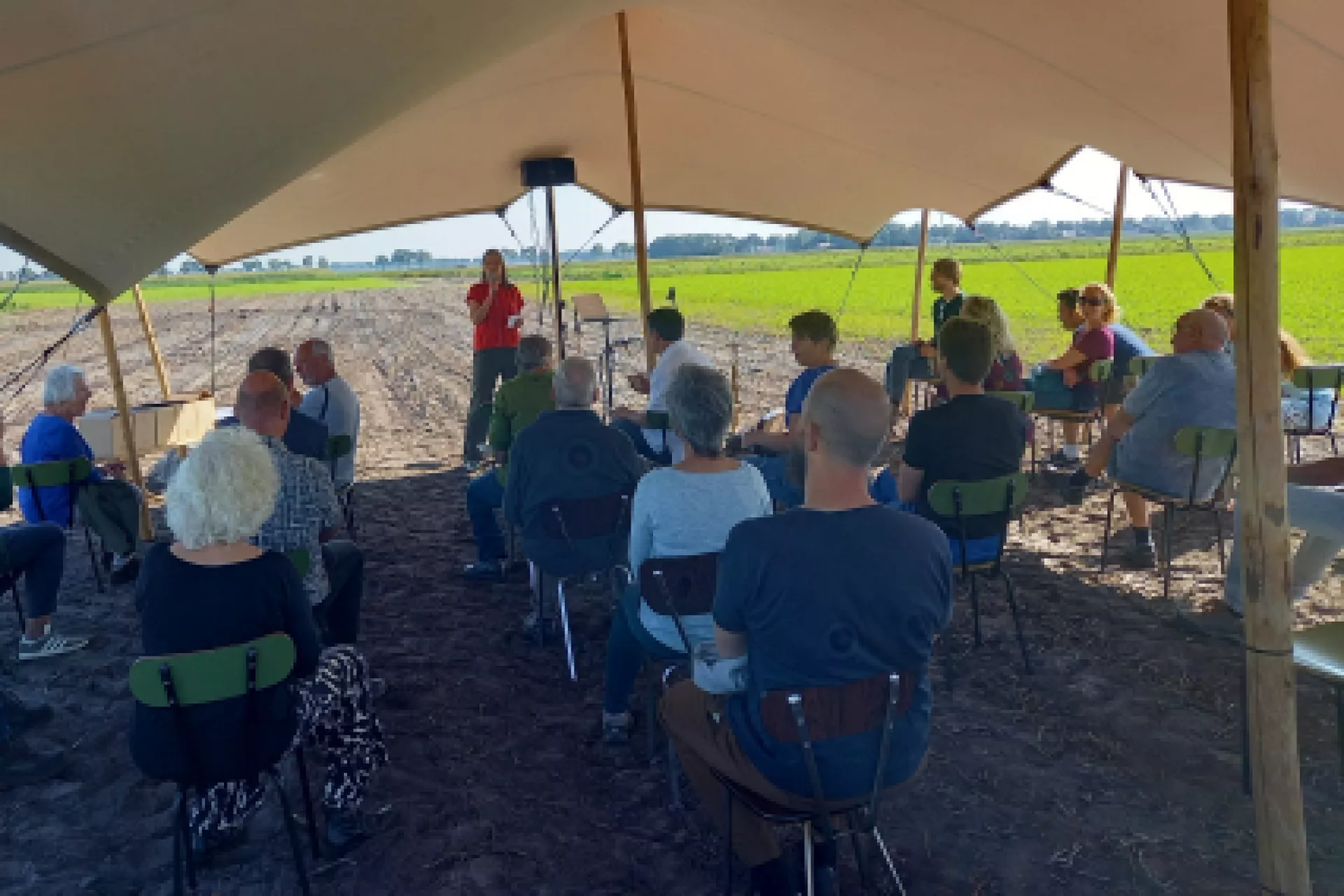 Groep mensen onder een tent op een veldbijeenkomst.