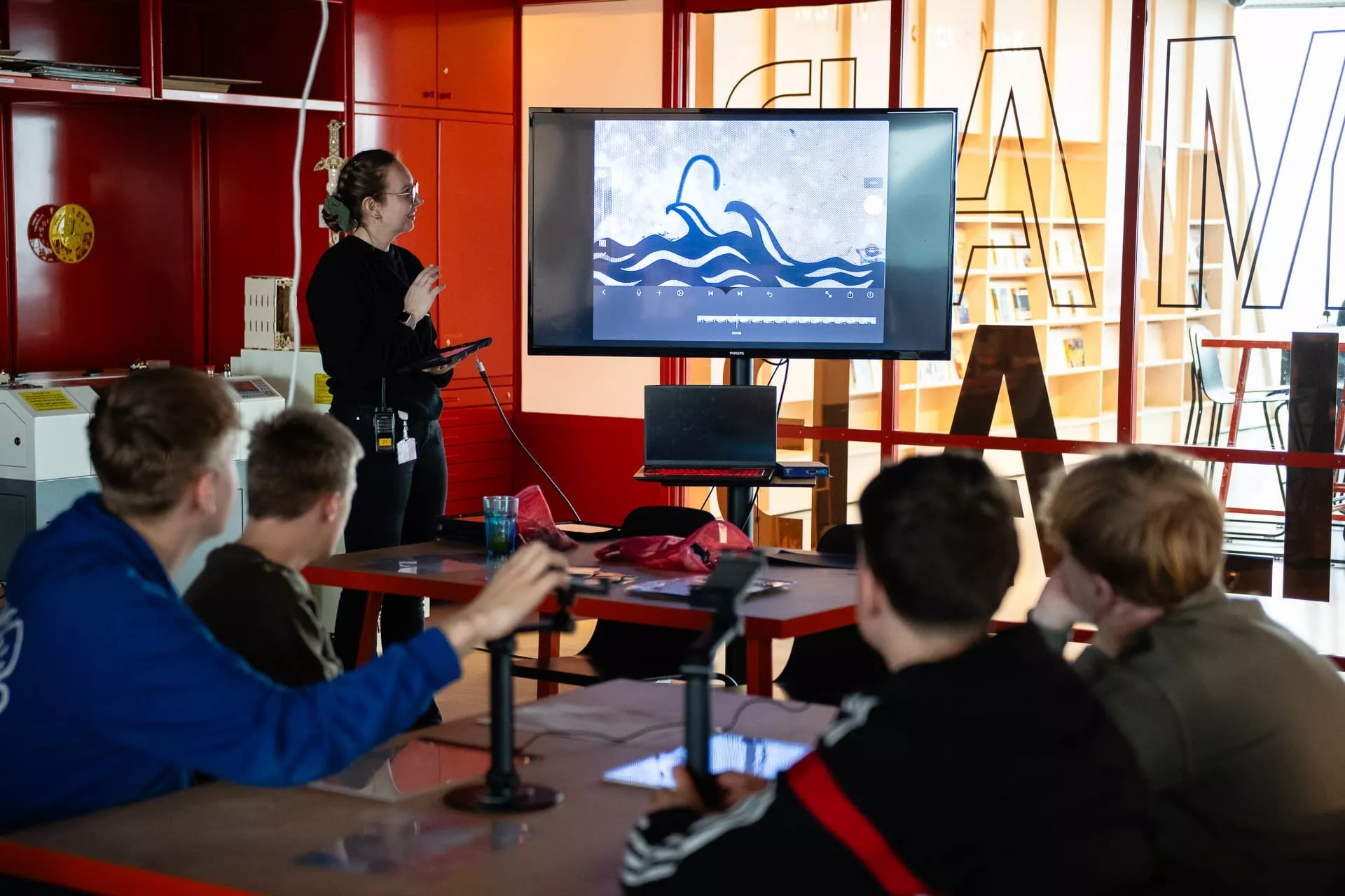 Een groep jongeren kijkt naar een presentatie op een scherm in een klaslokaal.