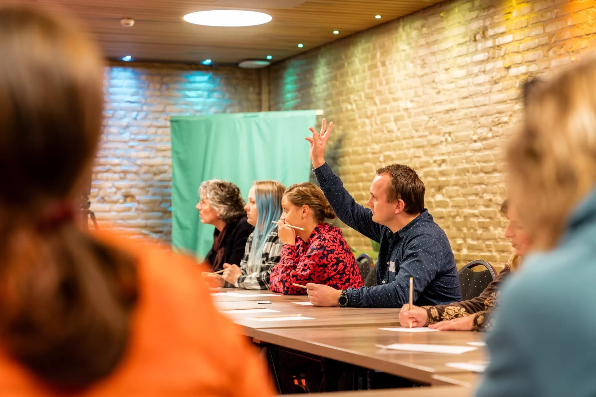 Een man steekt zijn hand op tijdens een cursus aan een lang tafel.