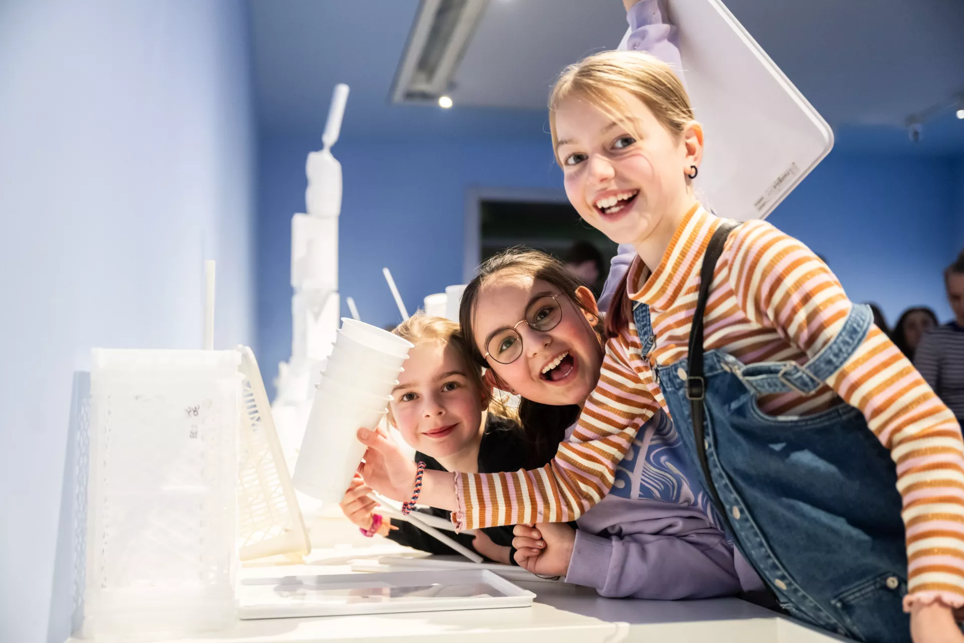Drie lachende kinderen genieten van een interactieve tentoonstelling.