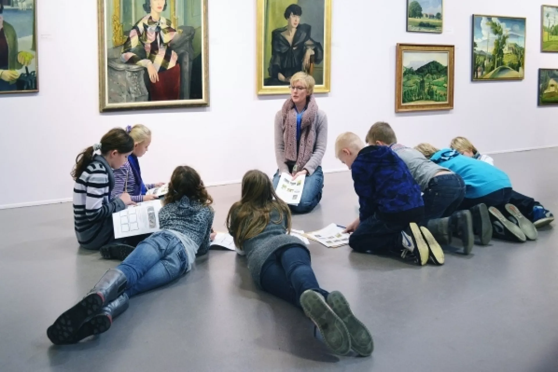 Kinderen liggen en zitten in een halve cirkel om de docent op de grond in een museum. 
