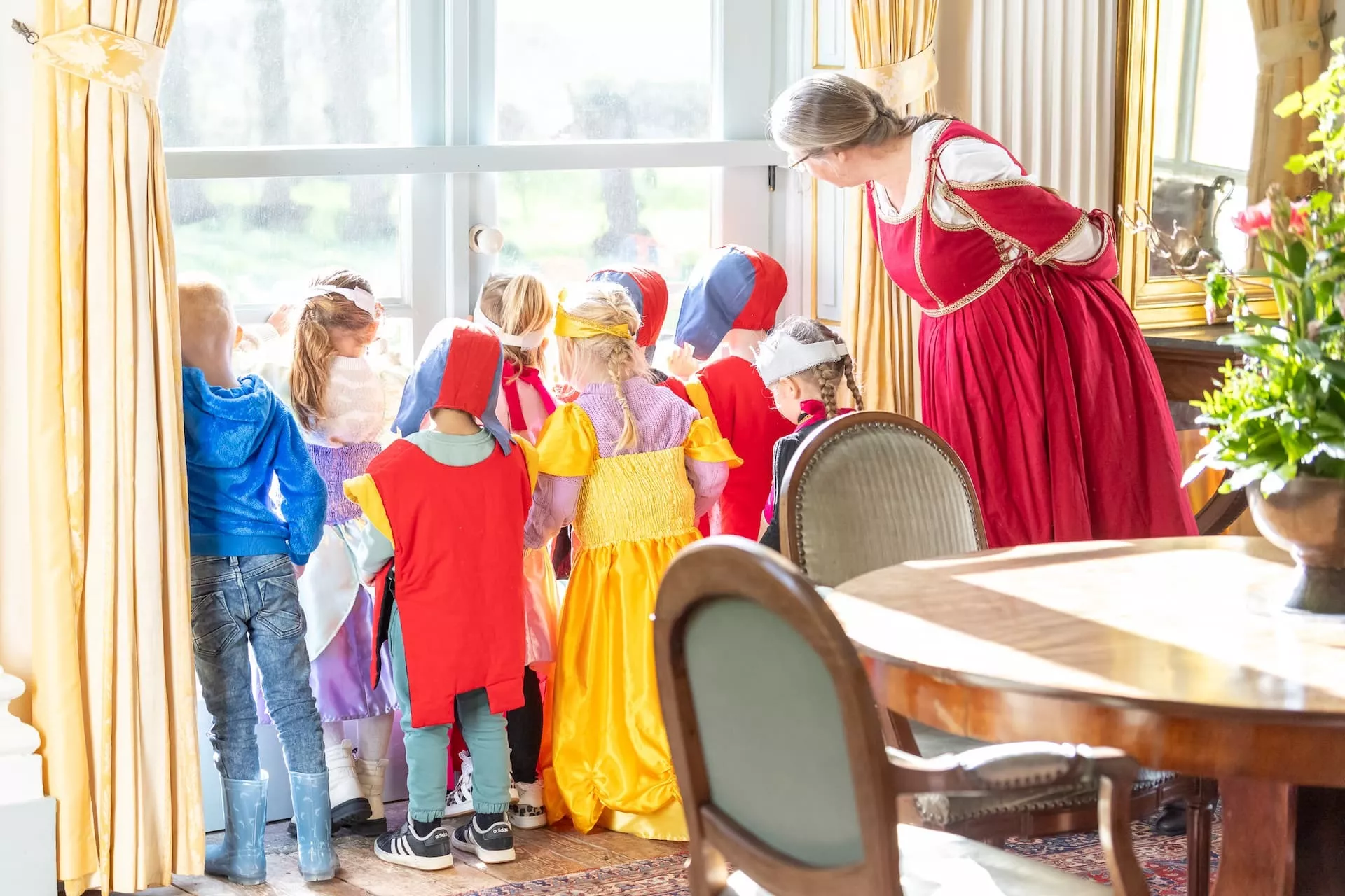 Kinderen en een volwassene in historische kostuums kijken nieuwsgierig uit het raam.