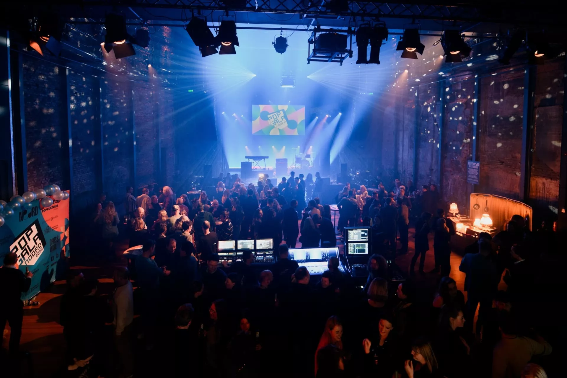 Een druk bezochte muziekruimte met een lichtshow en een projectiescherm.