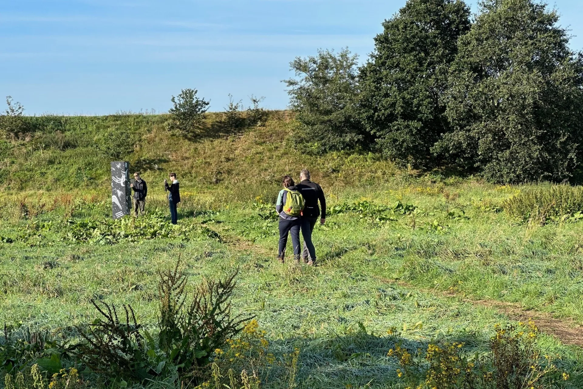 Mensen wandelen in een groen landschap met bomen en een monument op de achtergrond.