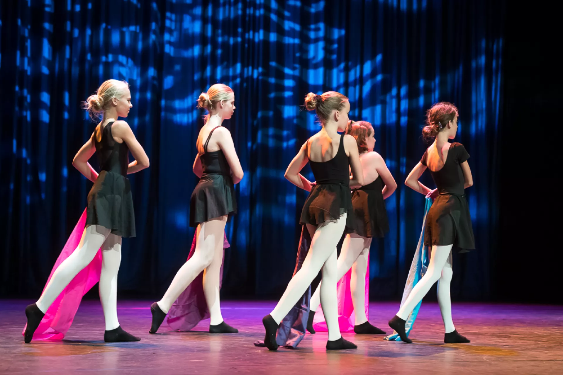 Groep jonge dansers in zwarte kostuums voert een choreografie uit op een podium.