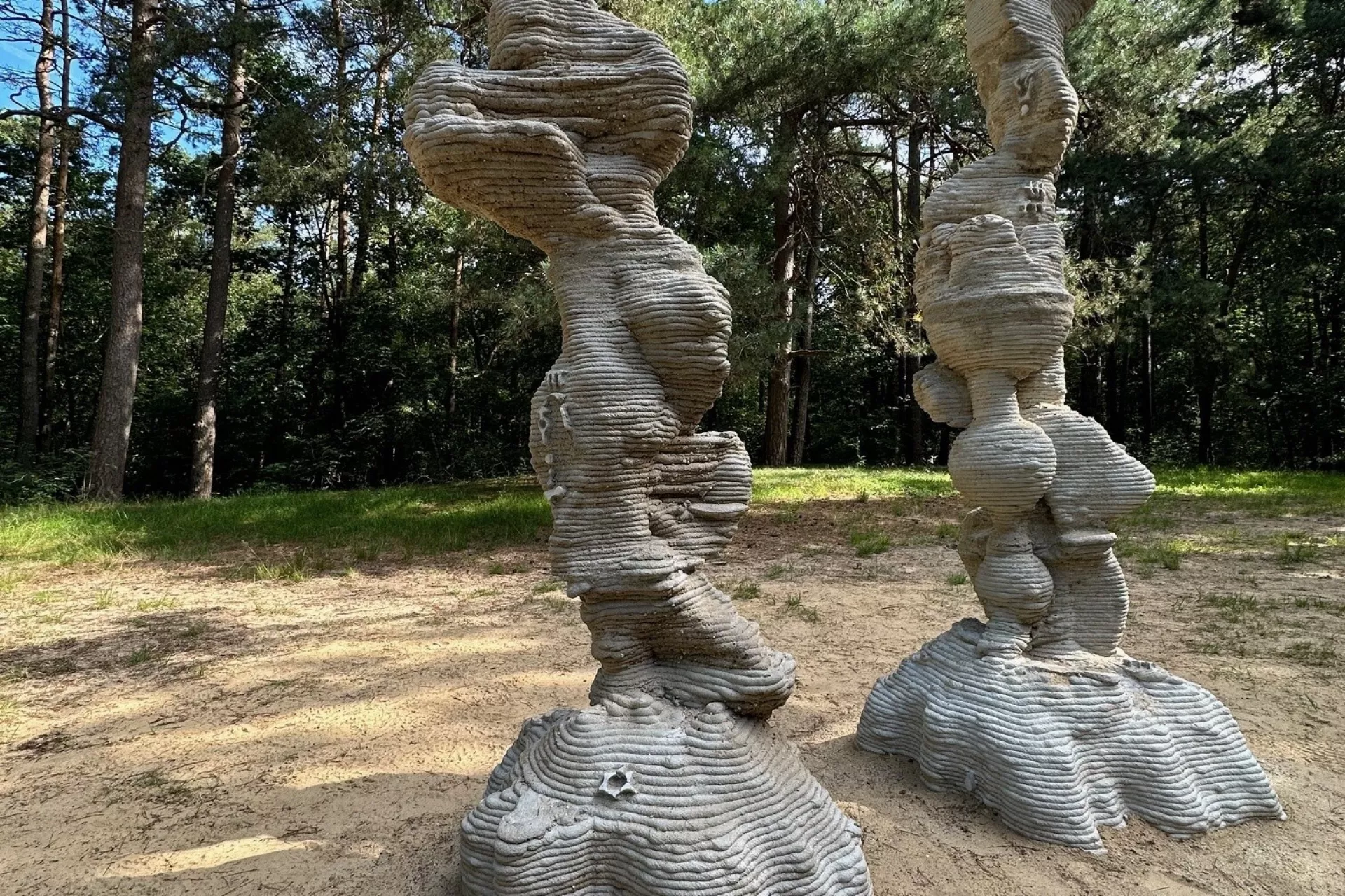 Twee gestapelde sculpturen in een bosrijke omgeving.