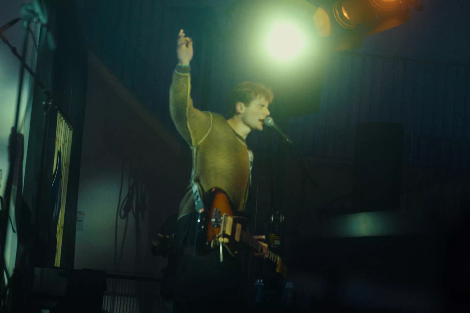 Een muzikant staat op het podium en zingt met een gitaar in de hand, verlicht door de spotlights.