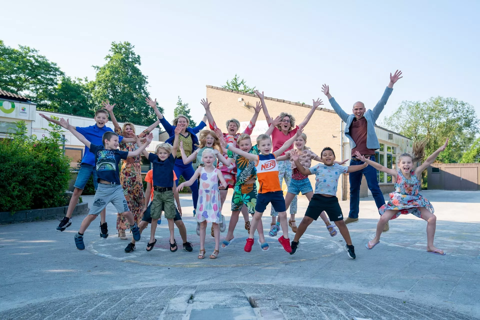 Groep kinderen en een volwassene springen vrolijk in de lucht op een zonnige dag.
