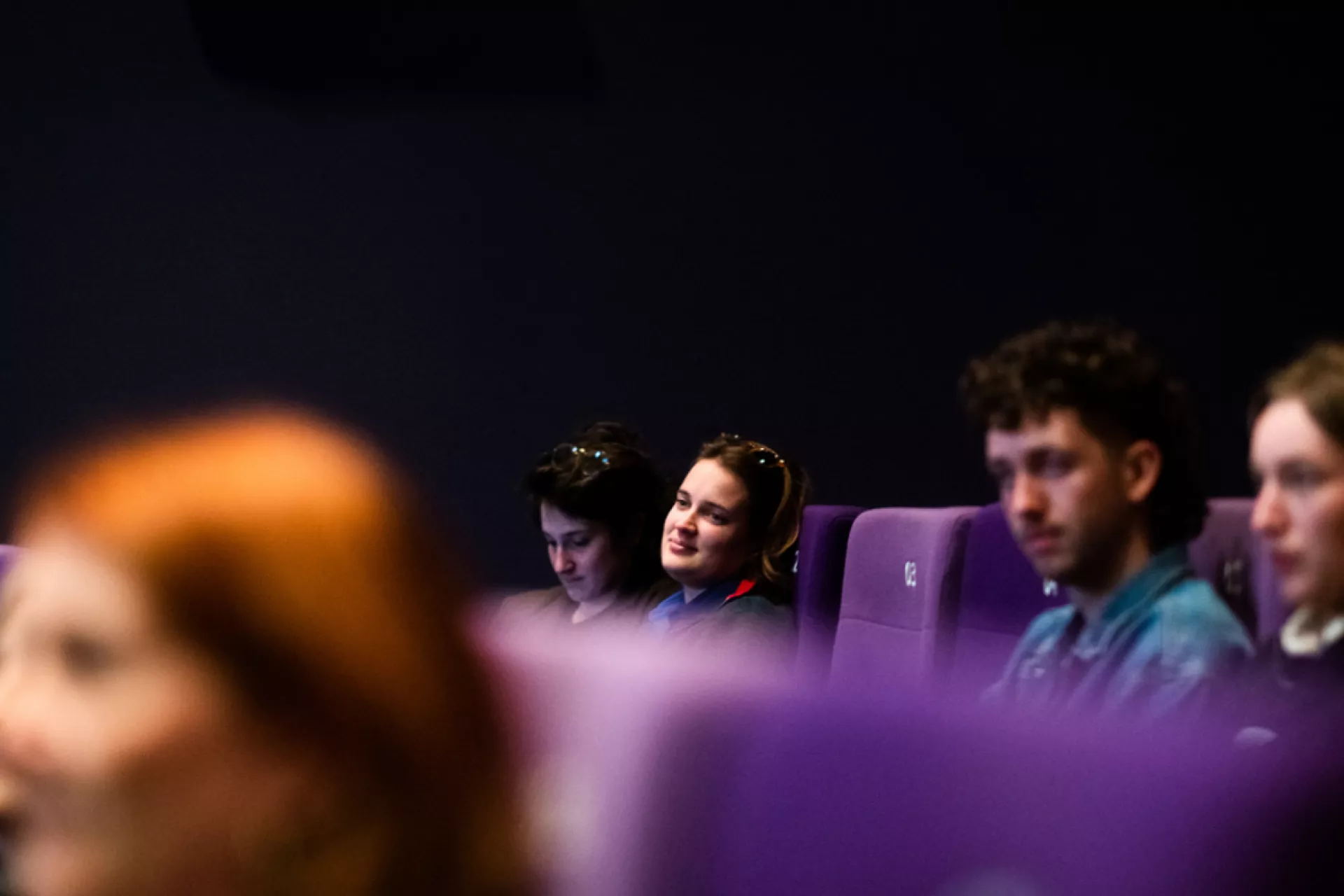 Mensen zitten in een bioscoopzaal met paarse stoelen.