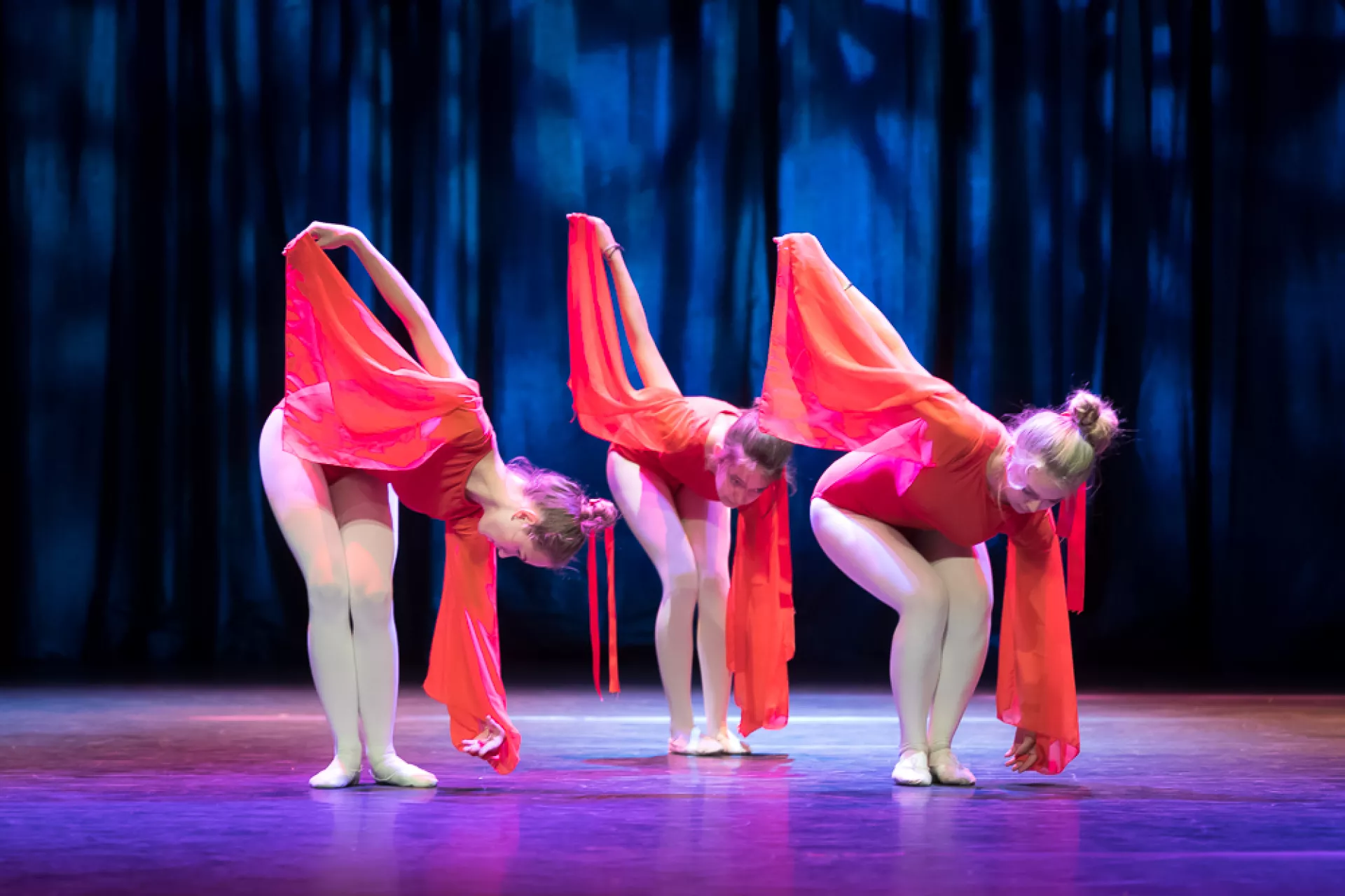Drie dansers in felrode kostuums buigen voorover op het podium.