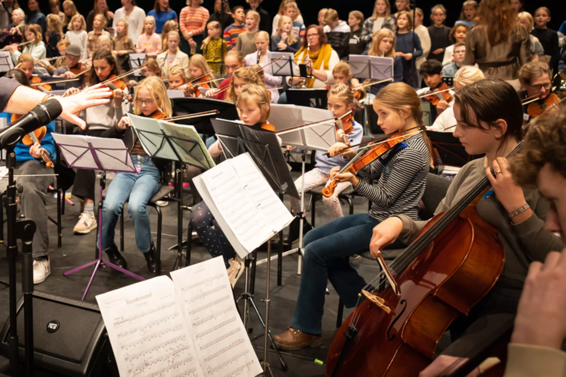 Dirigent leidt een orkest van muzikanten en koor op een podium.