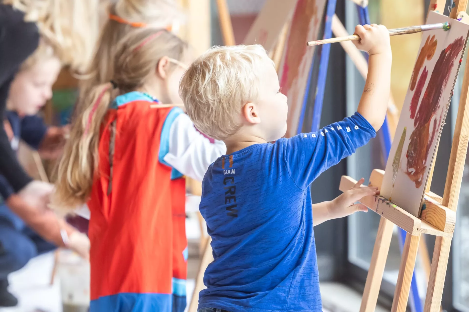 Je ziet twee kinderen die druk schilderen op een schildersezel.