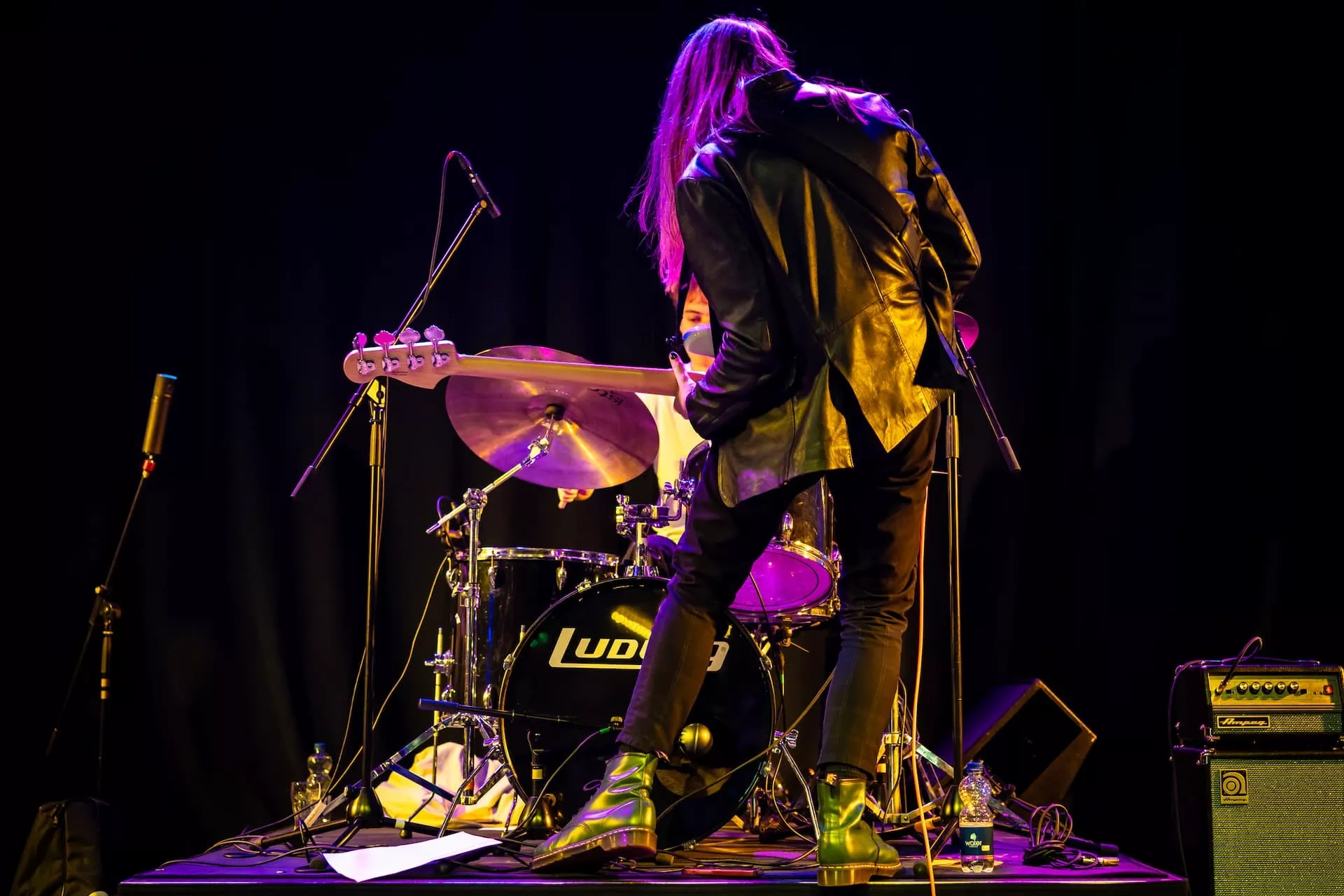 Muzikant speelt basgitaar op podium naast drumstel.
