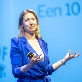 Een vrouw in een blauwe outfit geeft een presentatie op een podium.